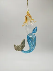 This product is a glass mermaid ornament with a blue and gold glitter finish. The mermaid's tail is made of blown glass and is decorated with glitter. The mermaid's hair is also made of blown glass and is decorated with glitter. The ornament is perfect for adding a touch of whimsy to your Christmas tree.