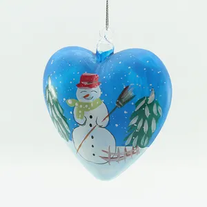 This heart-shaped glass ornament features a charming hand-painted snowman design against a blue wintery backdrop, perfect for adding a festive touch to your holiday decor.  The snowman is meticulously detailed, with a red hat, green scarf, and a friendly smile, making it a delightful addition to any Christmas tree.